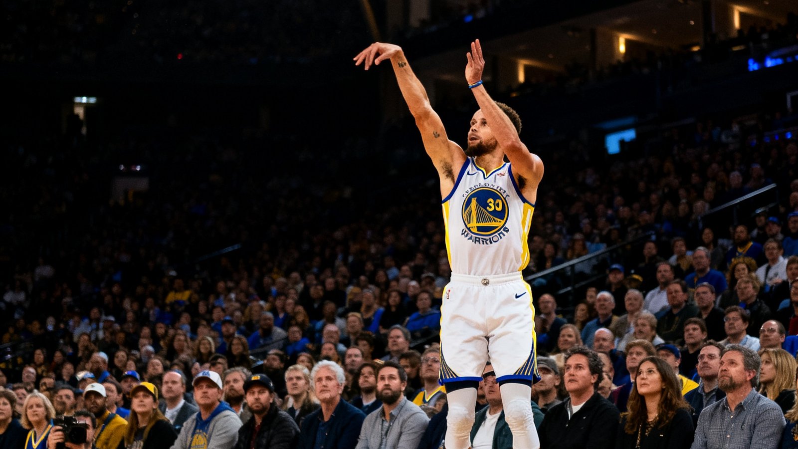 NBA赛场上斯蒂芬·库里在三分线外起跳投篮，篮球在空中划出弧线，全场观众屏息凝视的紧张瞬间